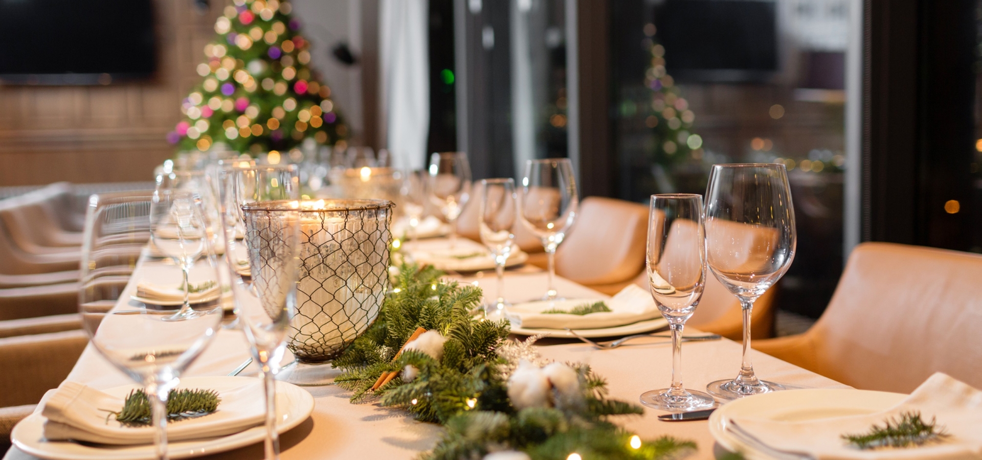 A long table set for a Christmas dinner with a Christmas tree in the background