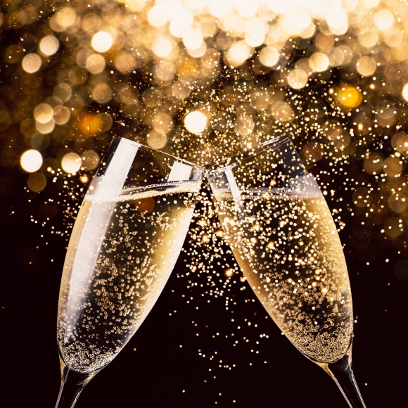 Two glasses of champagne toasting in the nigh with lights bokeh, glitter and sparks on the background